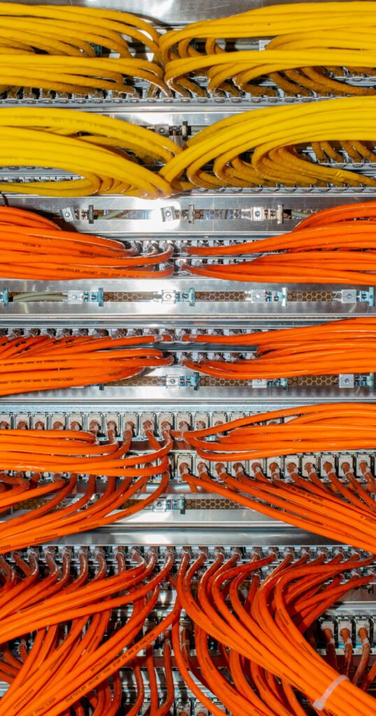 Um cabeamento estruturado, ou seja, vários cabos de rede amarelos e laranjas conectados em um switch de rede em um data center. Os cabos estão organizados em feixes e conectados a portas específicas no switch.