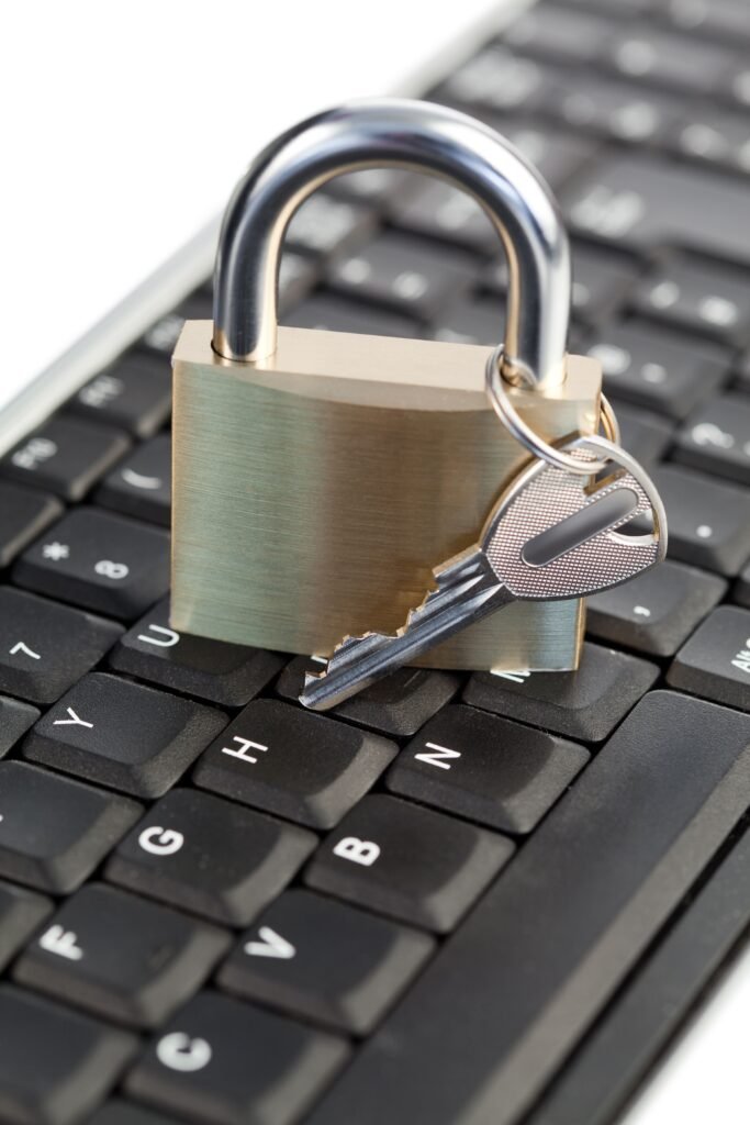 Um cadeado dourado de metal, com uma chave inserida, está de pé sobre um teclado preto de computador, simbolizando segurança da informação no meio digital.