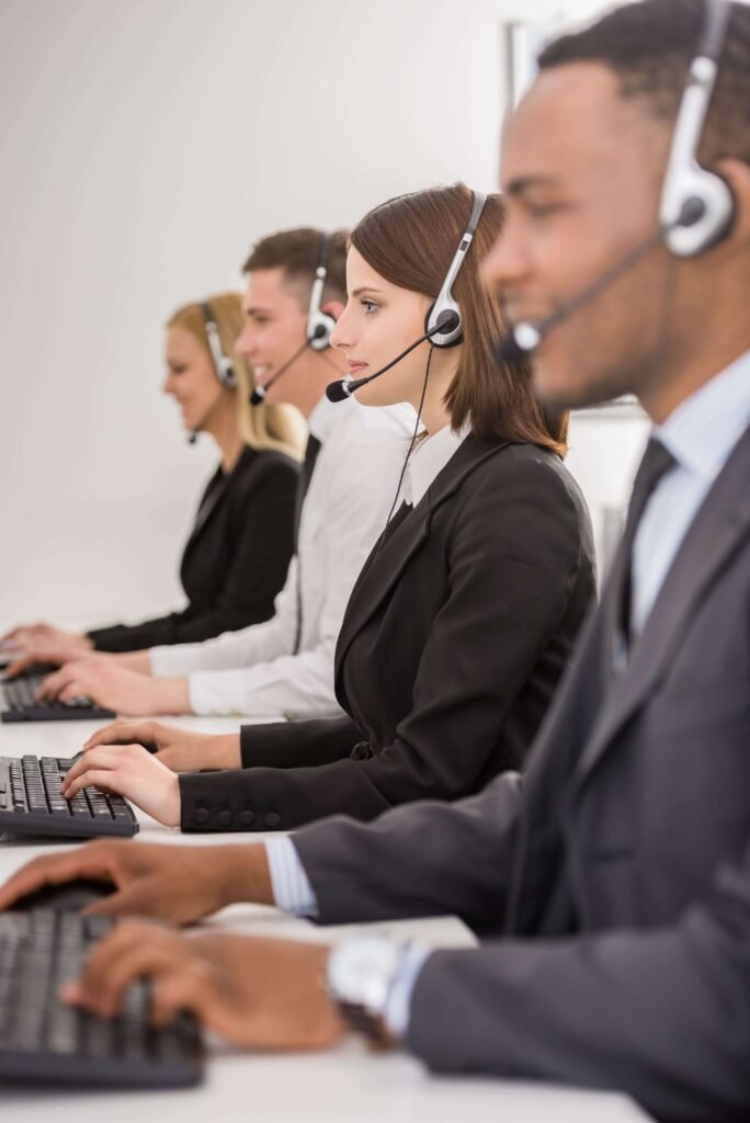 Quatro operadores de telemarketing usando fones de ouvido com microfone, trabalhando em computadores equipados com PABX Virtual em um ambiente de escritório. Eles estão alinhados em uma fileira, concentrados em suas tarefas.