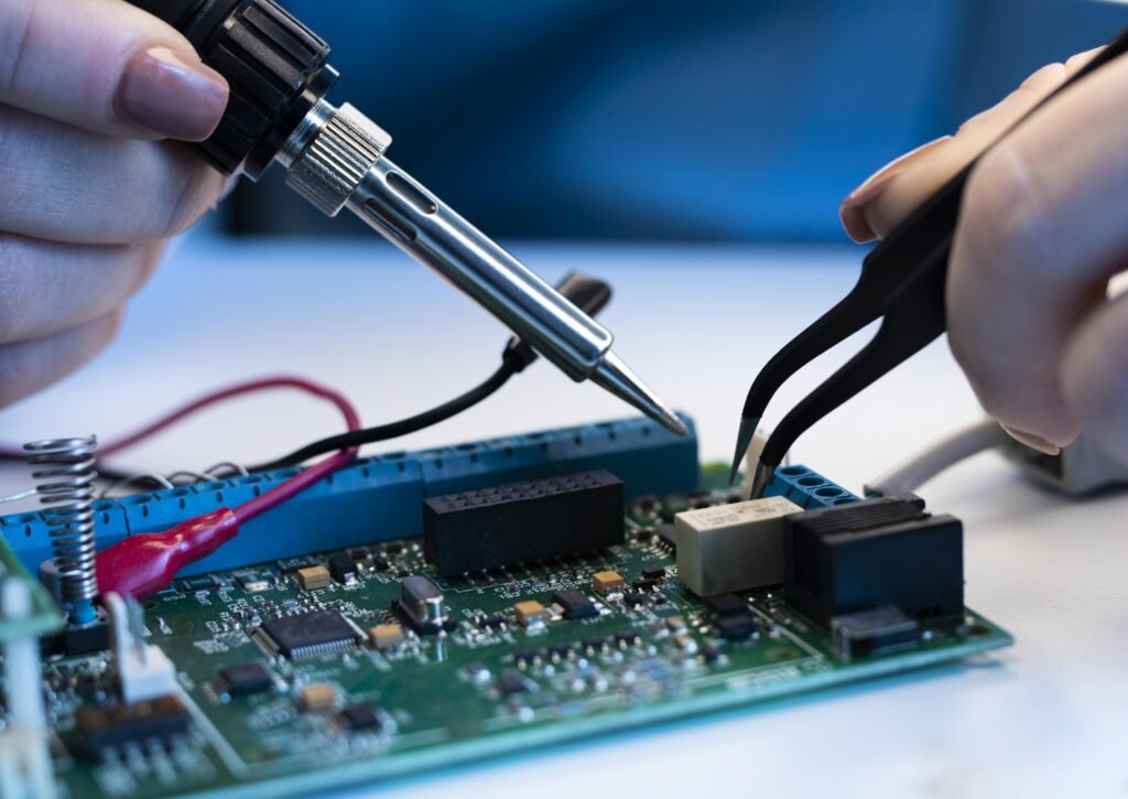 Duas mãos realizando a soldagem em uma placa de circuito eletrônico. Uma das mãos segura um ferro de solda enquanto a outra usa uma pinça para posicionar componentes. A imagem destaca a precisão necessária para o trabalho de manutenção eletrônica.