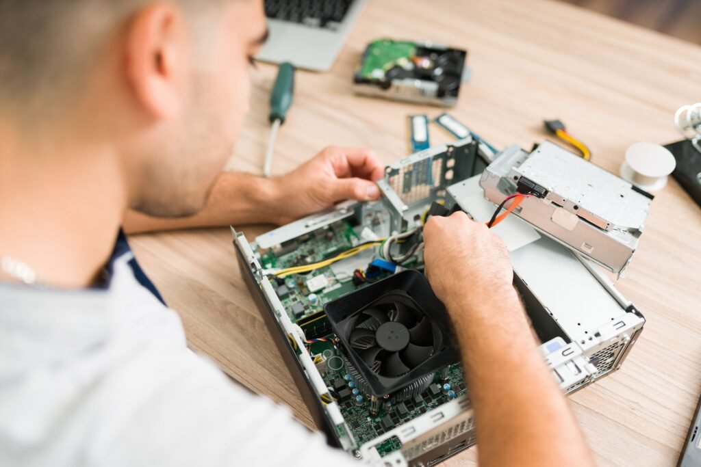 Um homem trabalhando na montagem interna de um computador desktop. Ele está encaixando um componente na placa-mãe, cercado por várias peças de hardware como a ventoinha, cabos e outros componentes eletrônicos sobre uma mesa de madeira.